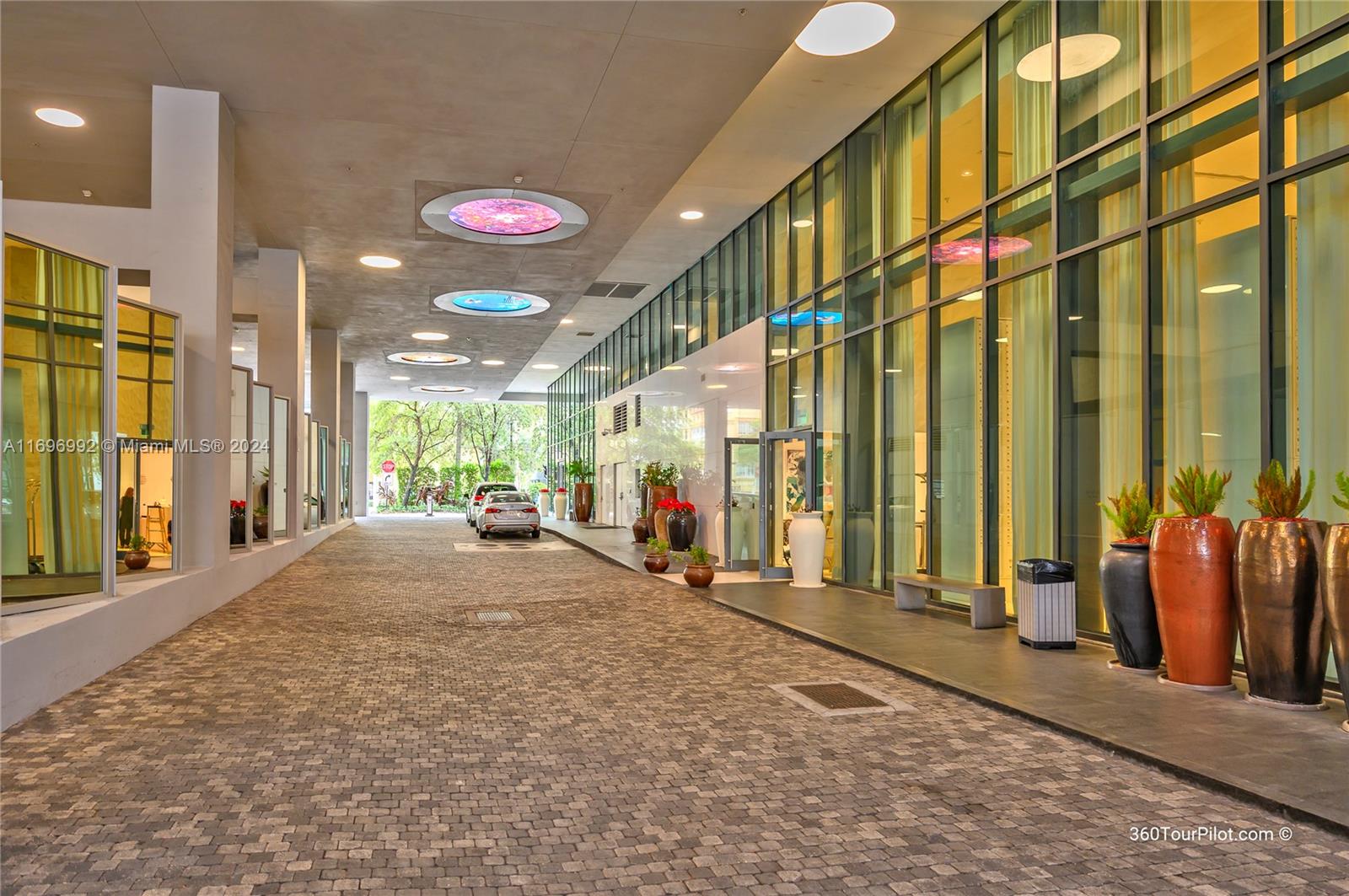 A paved driveway leads to a modern building entrance featuring glass walls and ceiling lights — 1300 S Miami Ave # 3704, Miami FL 33130, MIAMI, FL