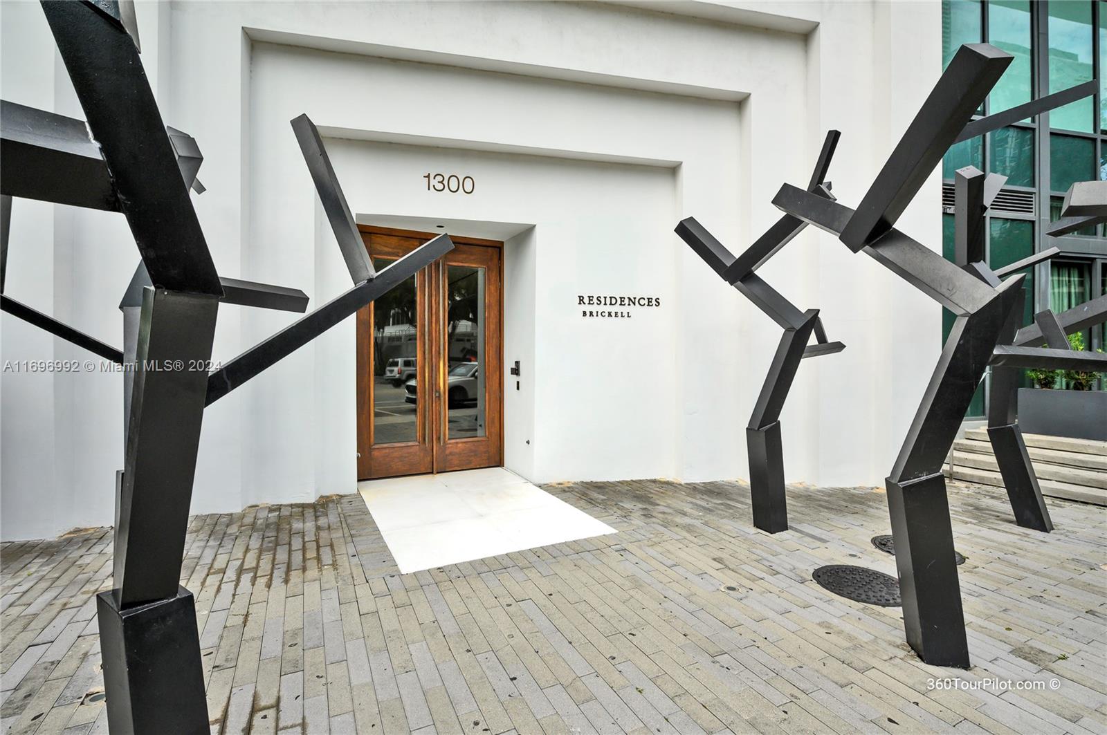 The entrance to a building features double wooden doors flanked by abstract black metal sculptures — 1300 S Miami Ave # 3704, Miami FL 33130, MIAMI, FL
