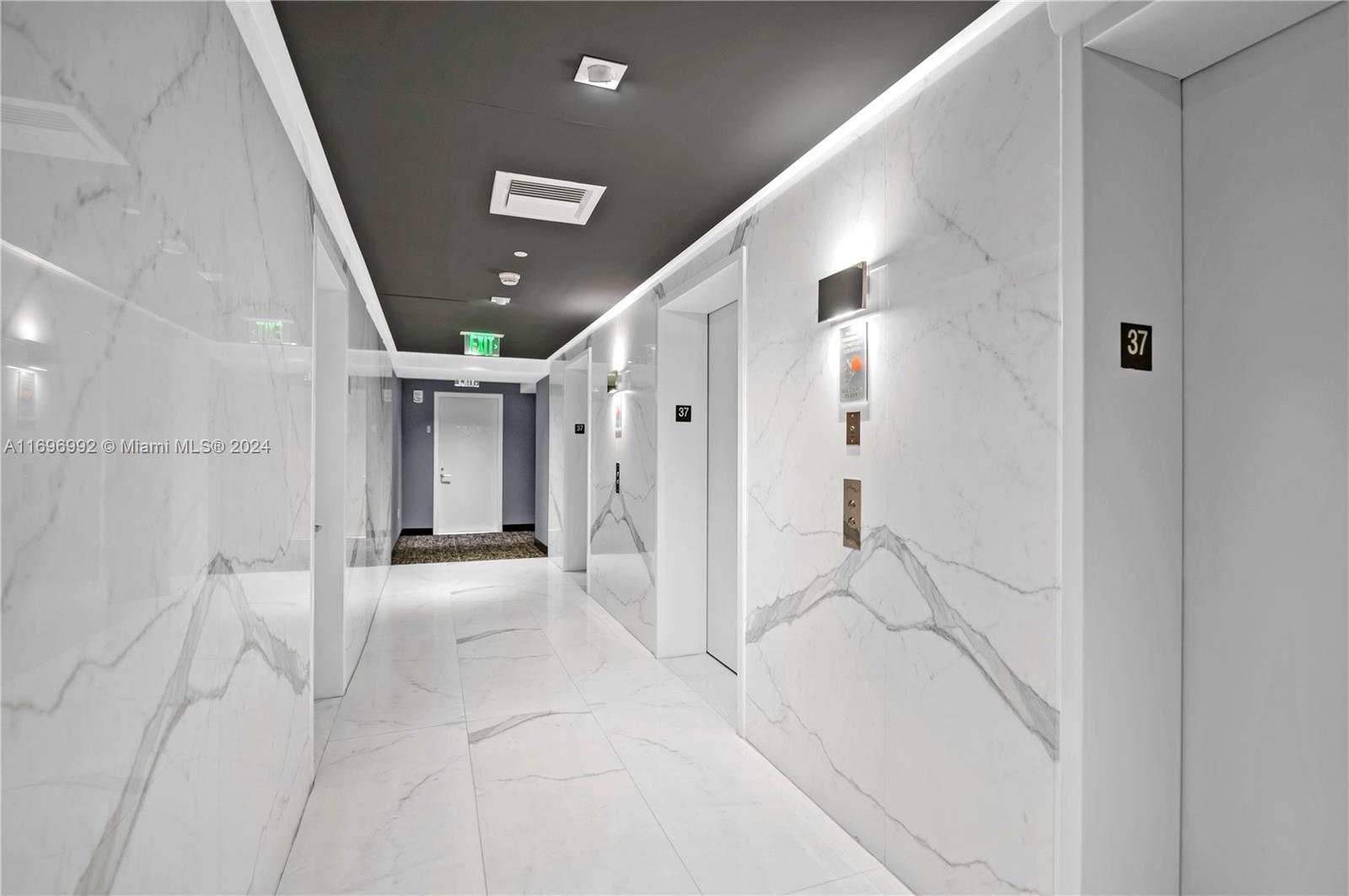 A modern hallway features white marble walls, tile flooring, and a dark grey ceiling — 1300 S Miami Ave # 3704, Miami FL 33130, MIAMI, FL