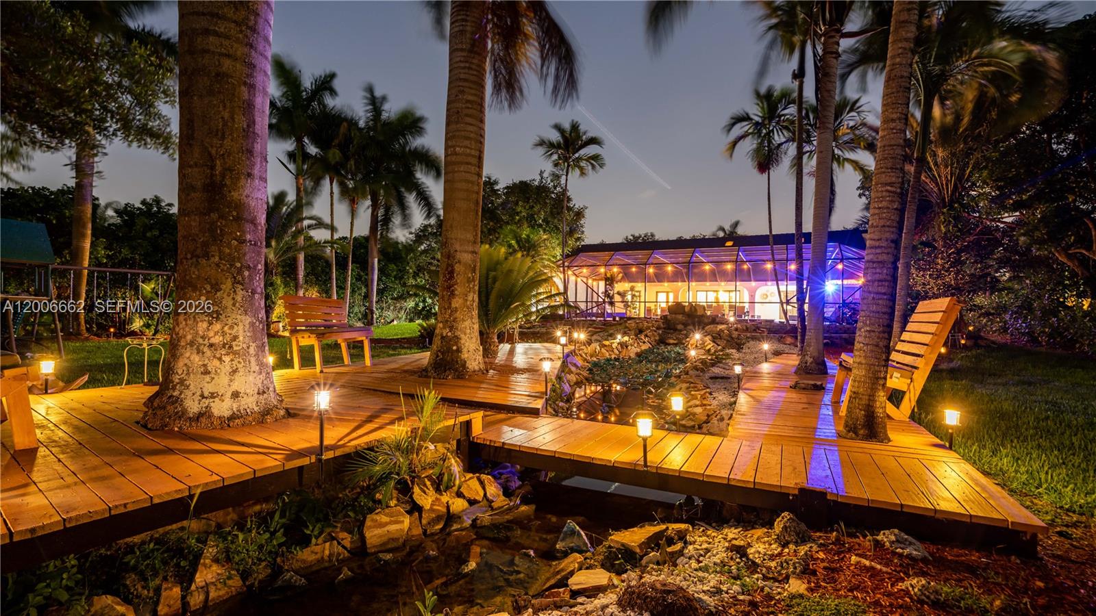 A wooden deck with a small pond and seating area sits in a palm-filled backyard — 1361 NW 116th Ave, Plantation FL 33323, PLANTATION, FL