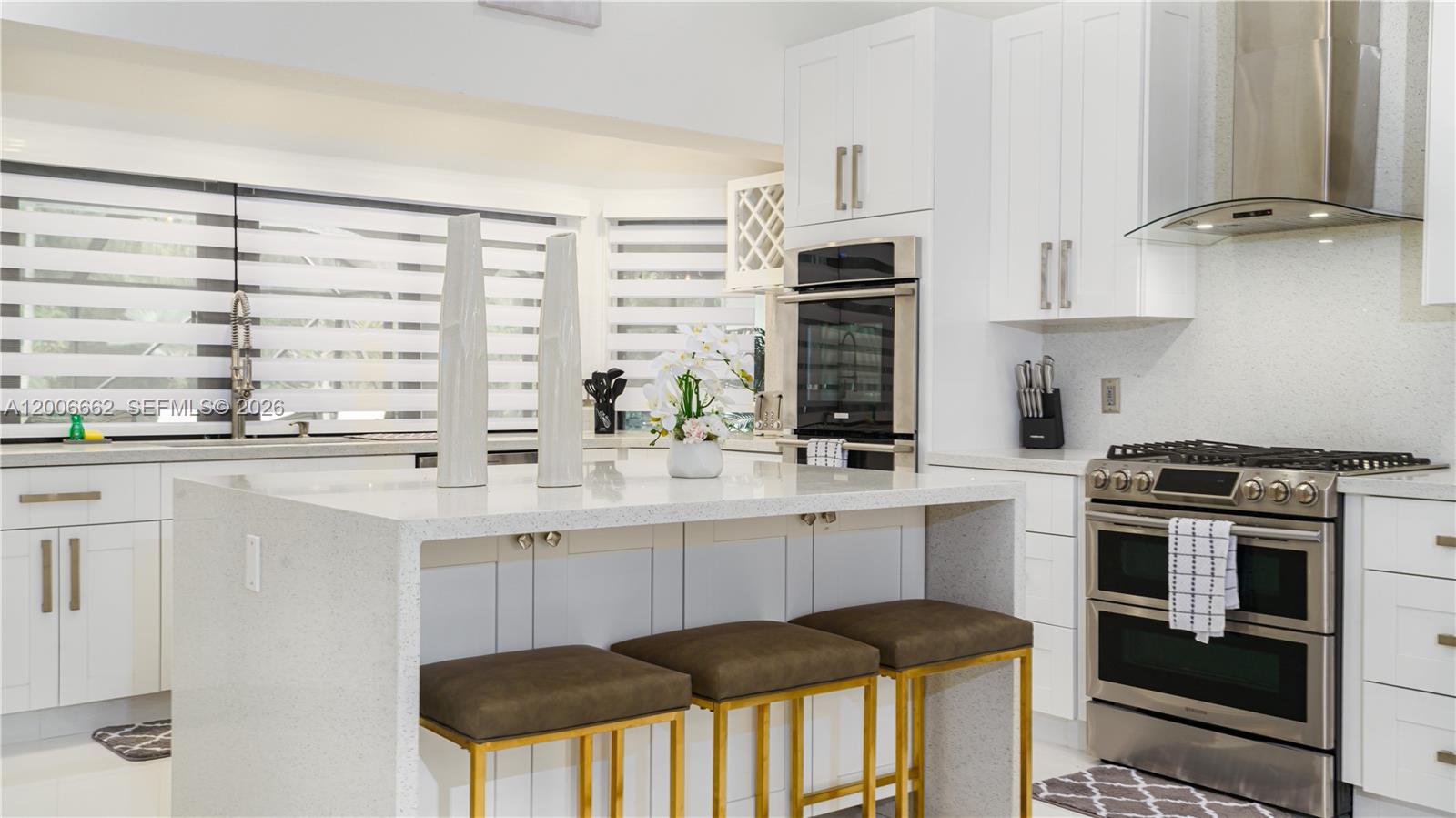 A modern kitchen features white cabinetry, a quartz waterfall island, and stainless steel appliances — 1361 NW 116th Ave, Plantation FL 33323, PLANTATION, FL