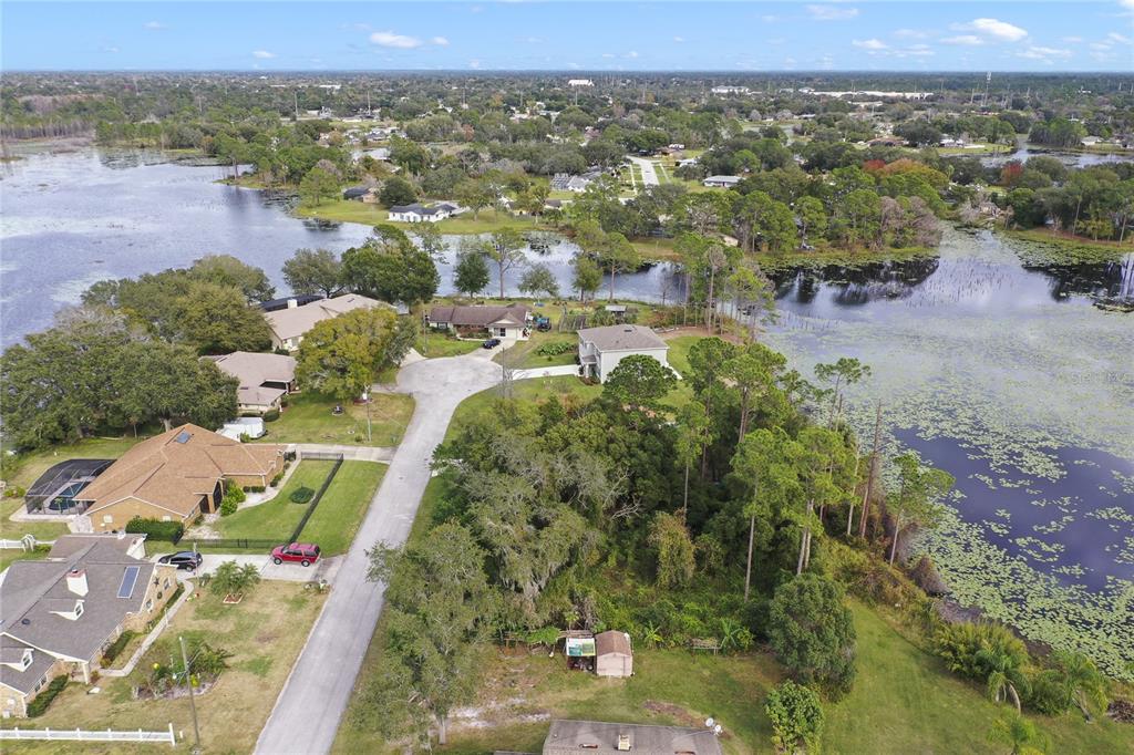 An aerial view shows a residential cul-de-sac surrounded by a large lake and trees — 2145 MONTECITO AVENUE, DELTONA, FL