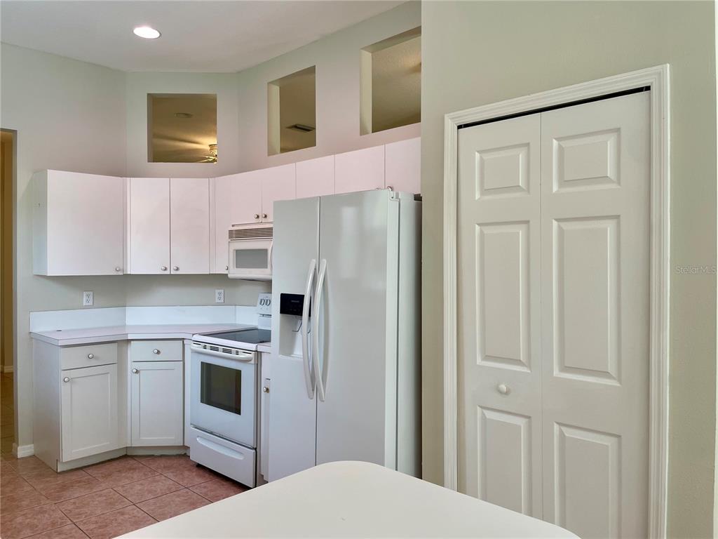 A kitchen features white cabinets, white appliances, and tiled flooring under high ceilings — 6813 WINSLOW STREET, SARASOTA, FL