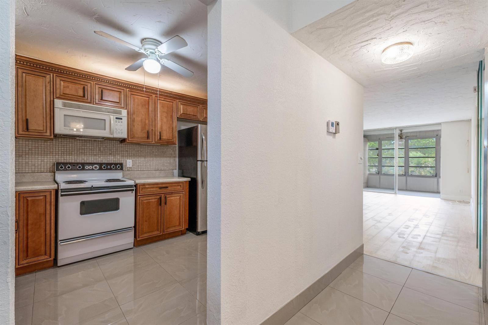 A kitchen with wood cabinets and white appliances opens into a living area with tile — 2551 Aragon Boulevard # 406, Sunrise FL 33322, SUNRISE, FL