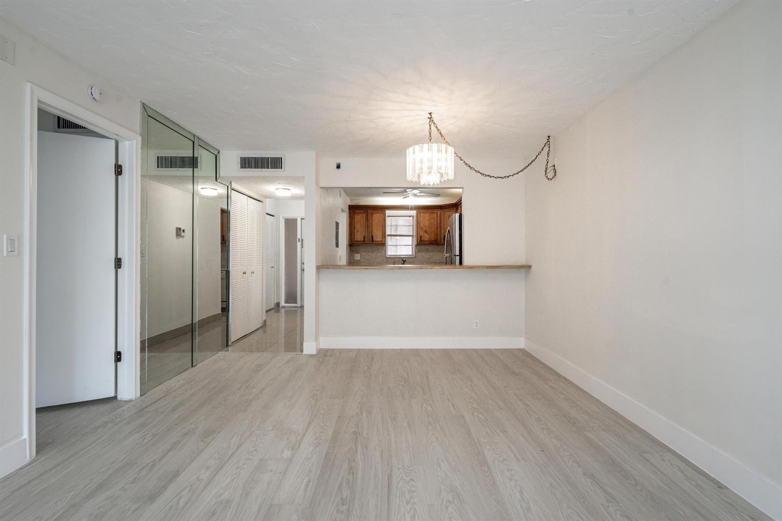 An empty room with light wood-look flooring, a mirrored wall, and a kitchen pass-through window — 2551 Aragon Boulevard # 406, Sunrise FL 33322, SUNRISE, FL