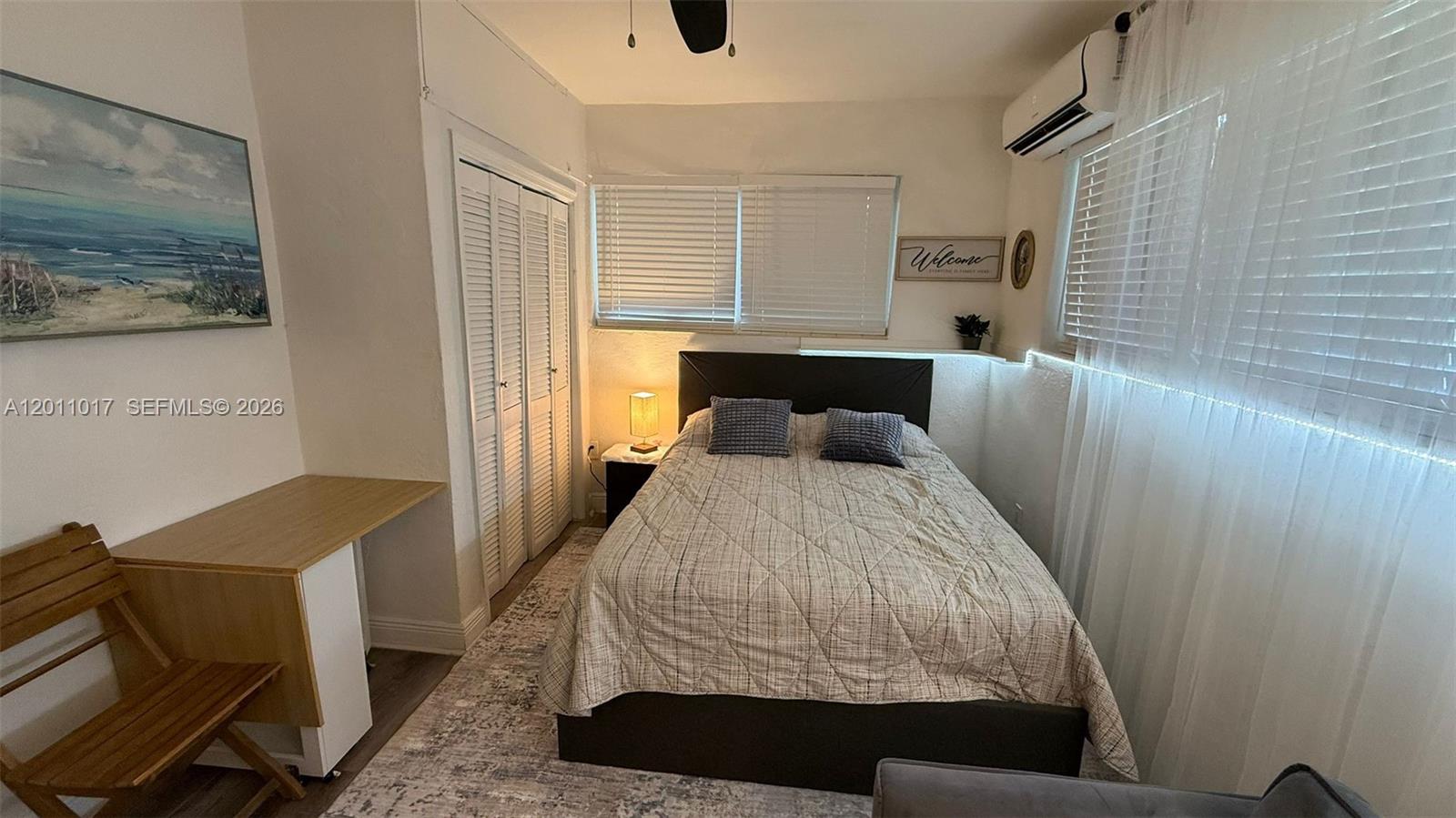 A bedroom features a bed with a patterned quilt, a desk, and louvered closet doors — 115 SE 2nd St # 2, Dania Beach FL 33004, DANIA BEACH, FL