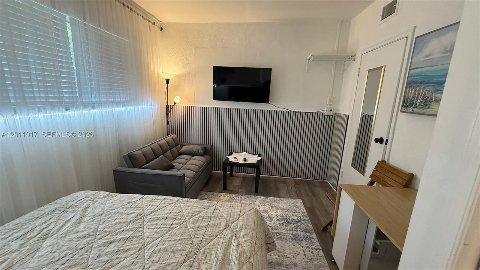 A bedroom features a bed, a grey sofa, a wall-mounted television, and striped wallpaper — 115 SE 2nd St # 2, Dania Beach FL 33004, DANIA BEACH, FL