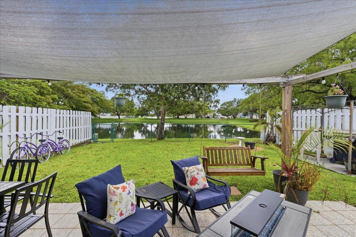 A backyard patio features a shade sail, outdoor furniture, and a view of a pond — 970 SW 111th Way, Davie FL 33324, DAVIE, FL