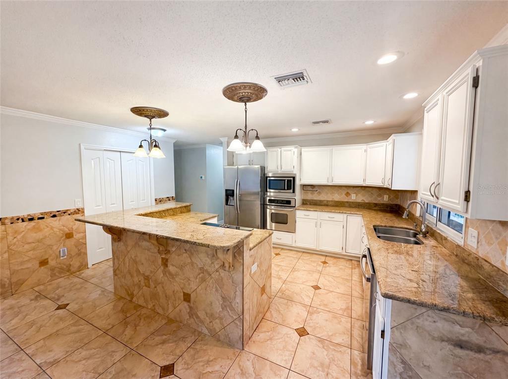 A kitchen features white cabinets, granite countertops, and tiled floors with a central island — 300 SPRUCEWOOD ROAD, LAKE MARY, FL