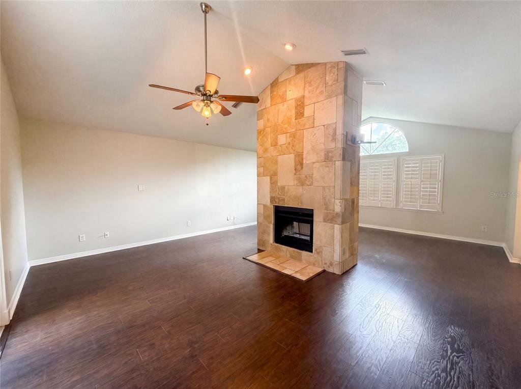 A living room features dark wood flooring, a vaulted ceiling, and a central stone fireplace — 300 SPRUCEWOOD ROAD, LAKE MARY, FL