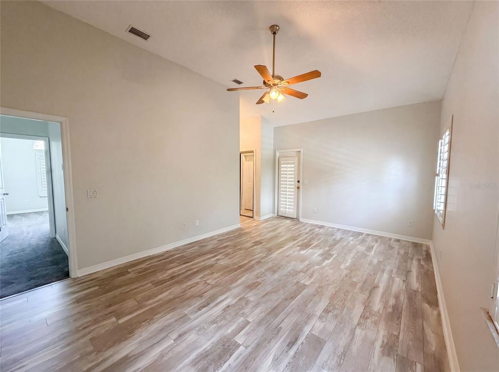 An empty room features light wood-look flooring, a vaulted ceiling with a fan, and white walls — 300 SPRUCEWOOD ROAD, LAKE MARY, FL