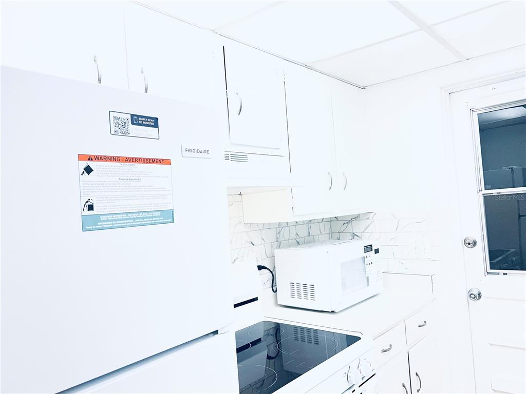A white kitchen features a Frigidaire refrigerator, a microwave, and marble-patterned backsplash tiles — 5467 HANSEL AVENUE UNIT H15, ORLANDO, FL