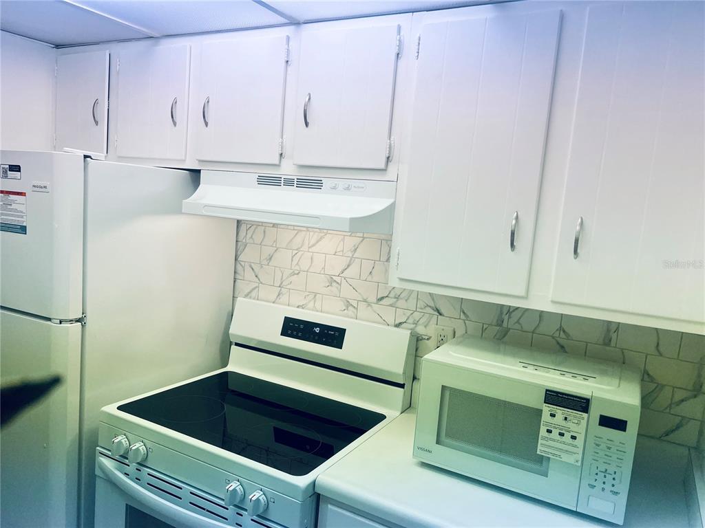 A white kitchen features white cabinets, a glass-top stove, and a white microwave — 5467 HANSEL AVENUE UNIT H15, ORLANDO, FL