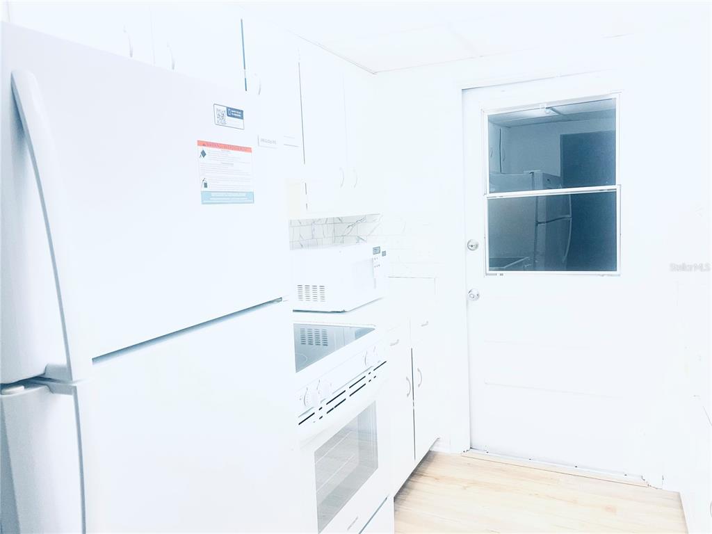 A bright kitchen features white cabinets, white appliances, and a door with a window — 5467 HANSEL AVENUE UNIT H15, ORLANDO, FL