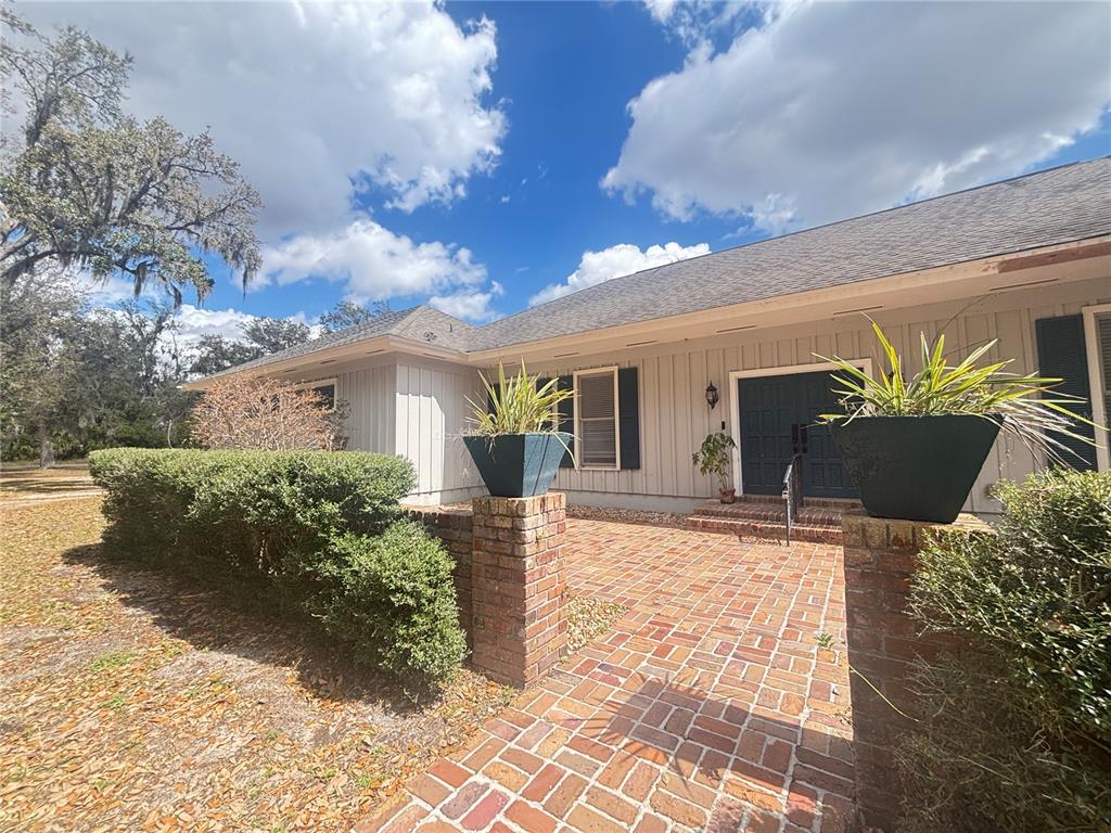 A brick walkway leads to the front entrance of a house with vertical siding — 1508 N ARCADIA AVENUE, ARCADIA, FL