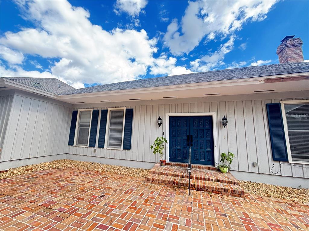 A house exterior with vertical gray siding, blue shutters, double doors, and a brick patio — 1508 N ARCADIA AVENUE, ARCADIA, FL