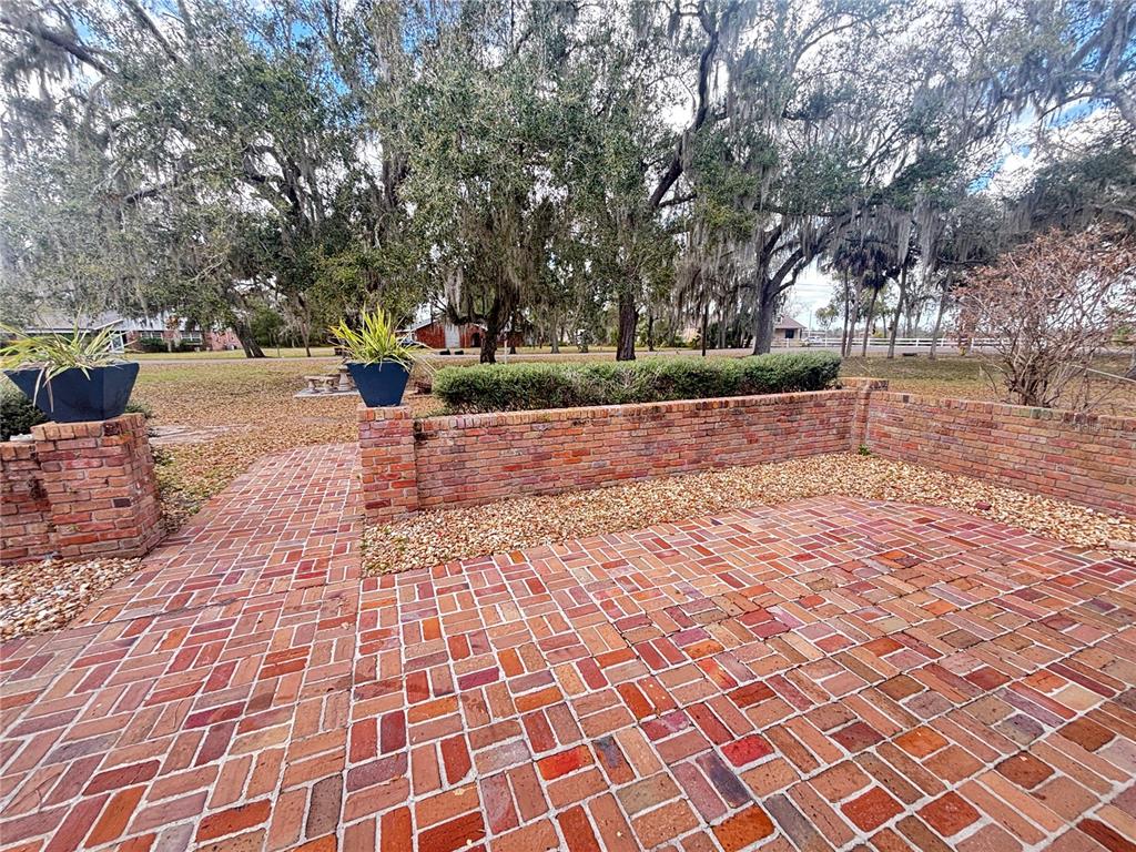 A brick patio features a low retaining wall, potted plants, and mature trees in the background — 1508 N ARCADIA AVENUE, ARCADIA, FL