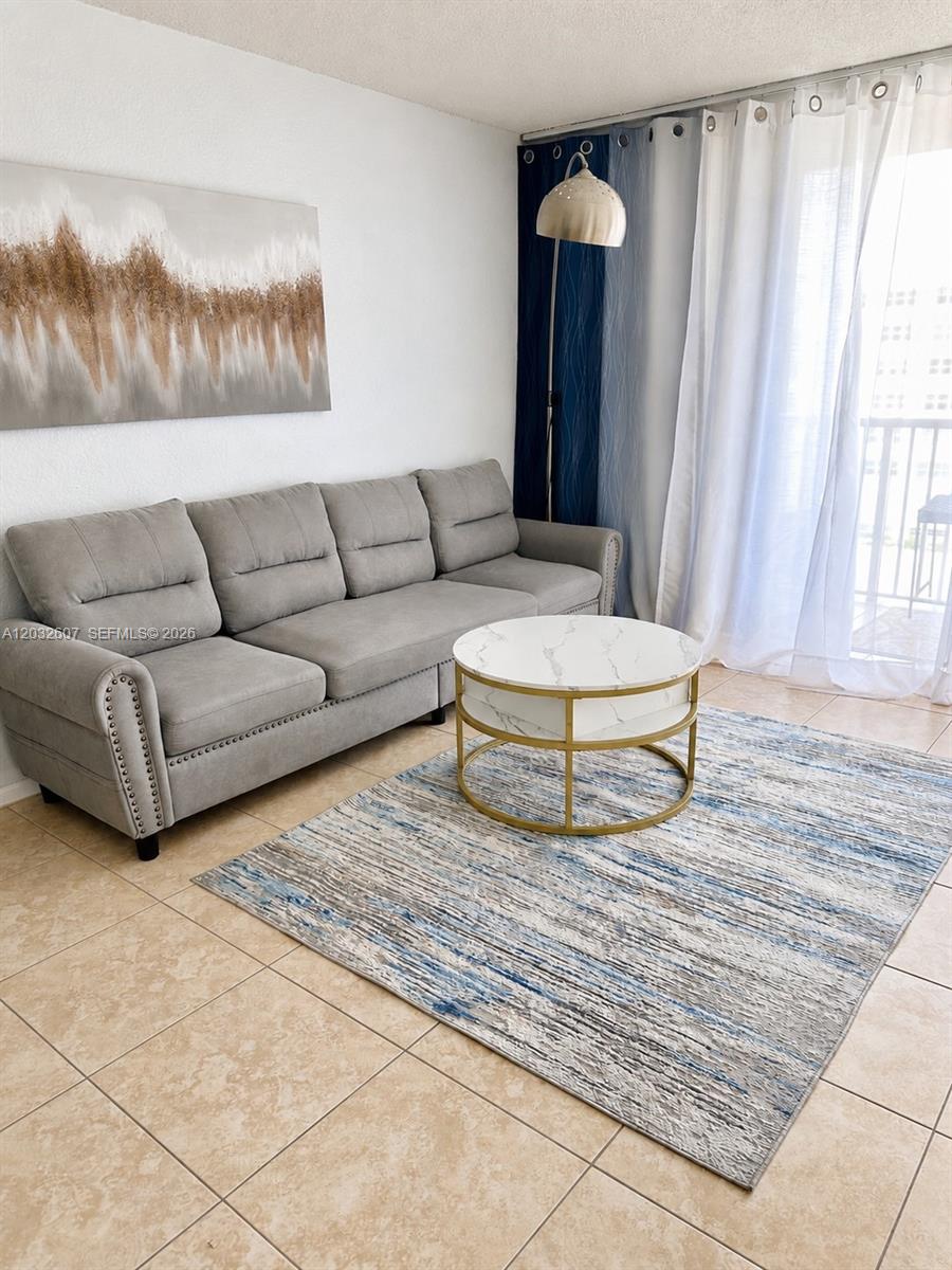 A living room features a grey sofa, a round marble coffee table, and blue curtains — 3161 S Ocean Dr # 803, Hallandale Beach FL 33009, HALLANDALE BEACH, FL