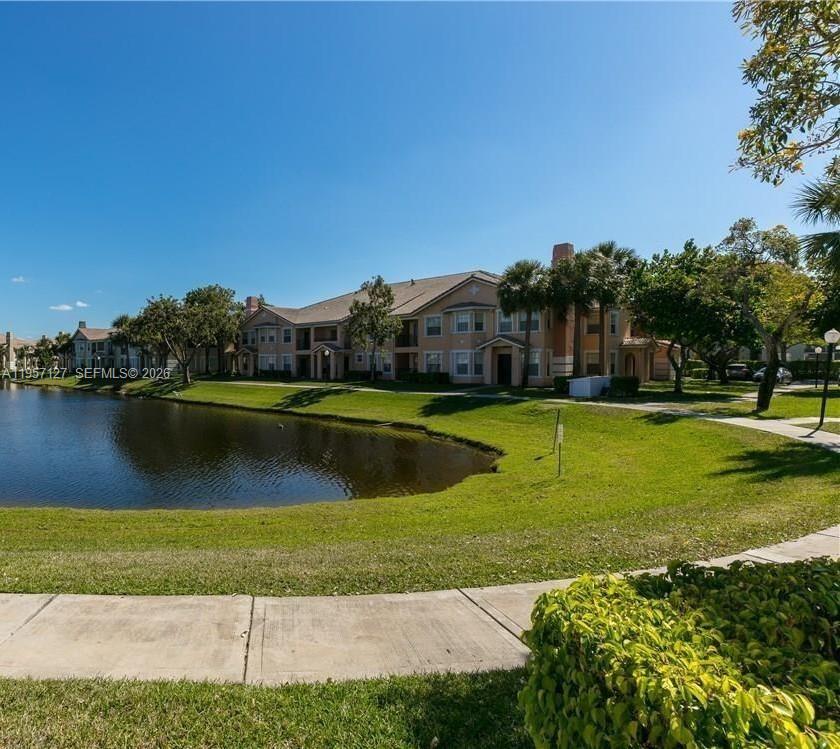A multi-story apartment building sits behind a pond with a grassy lawn and sidewalk — NORTH LAUDERDALE, FL