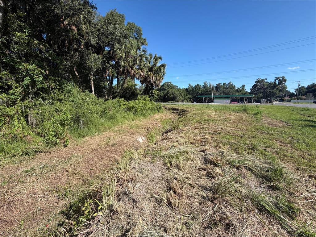 A grassy, uneven lot with a drainage ditch leads toward a distant gas station — DOSSEY ROAD S, LAKELAND, FL