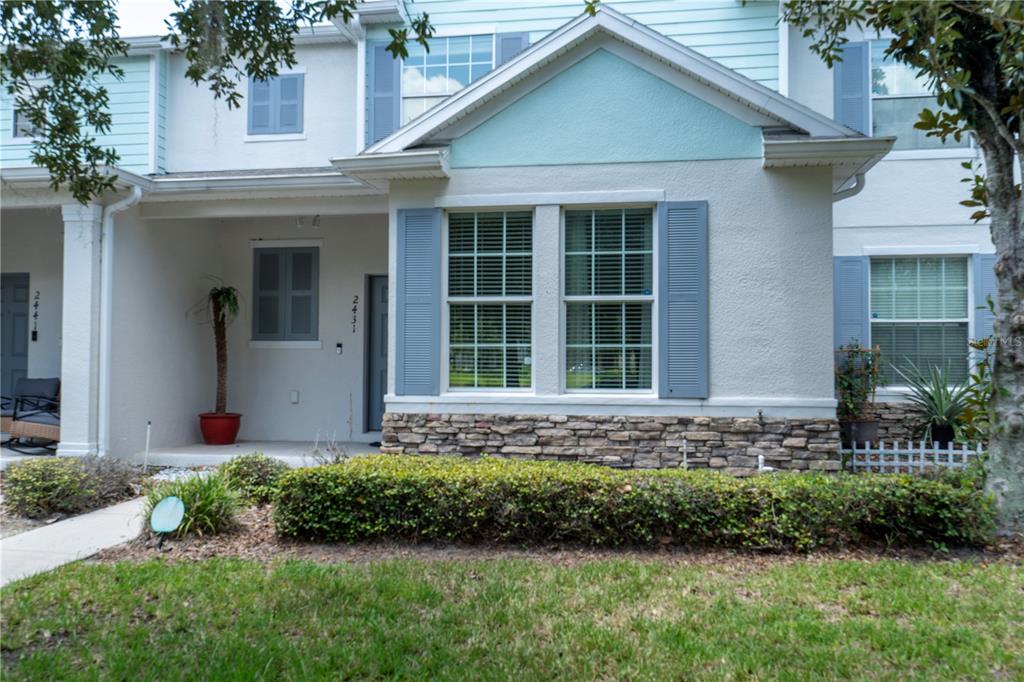 The exterior of a two-story townhouse features light-colored stucco, stone veneer, and blue shutters — 2431 GRASMERE VIEW PARKWAY N, KISSIMMEE, FL