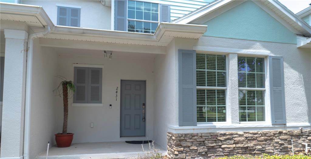 The exterior of a house features a covered porch, a gray front door, and stone siding — 2431 GRASMERE VIEW PARKWAY N, KISSIMMEE, FL
