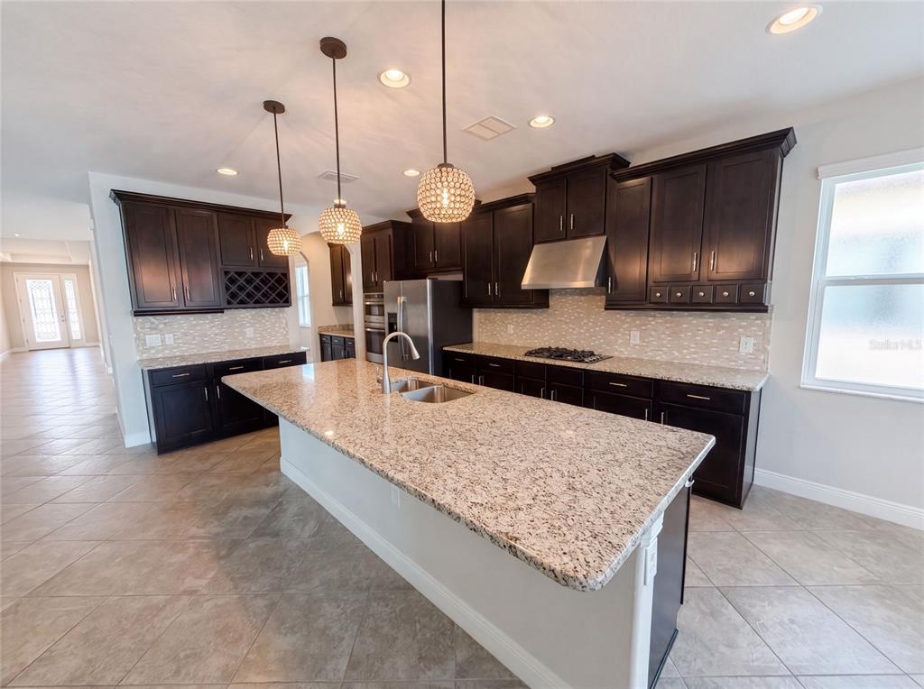 A kitchen features dark wood cabinets, granite countertops, a central island, and three pendant lights — 2575 GRAND LAKESIDE DRIVE, PALM HARBOR, FL