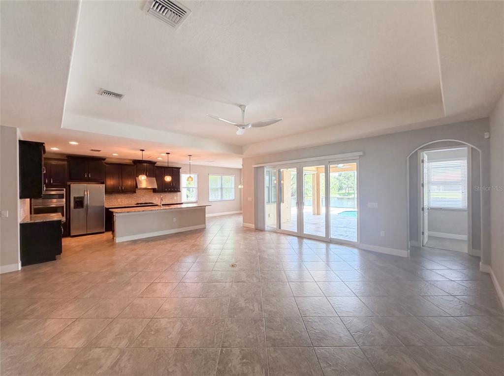 A spacious open-concept living area features tile flooring, a kitchen with dark cabinets, and sliding doors — 2575 GRAND LAKESIDE DRIVE, PALM HARBOR, FL