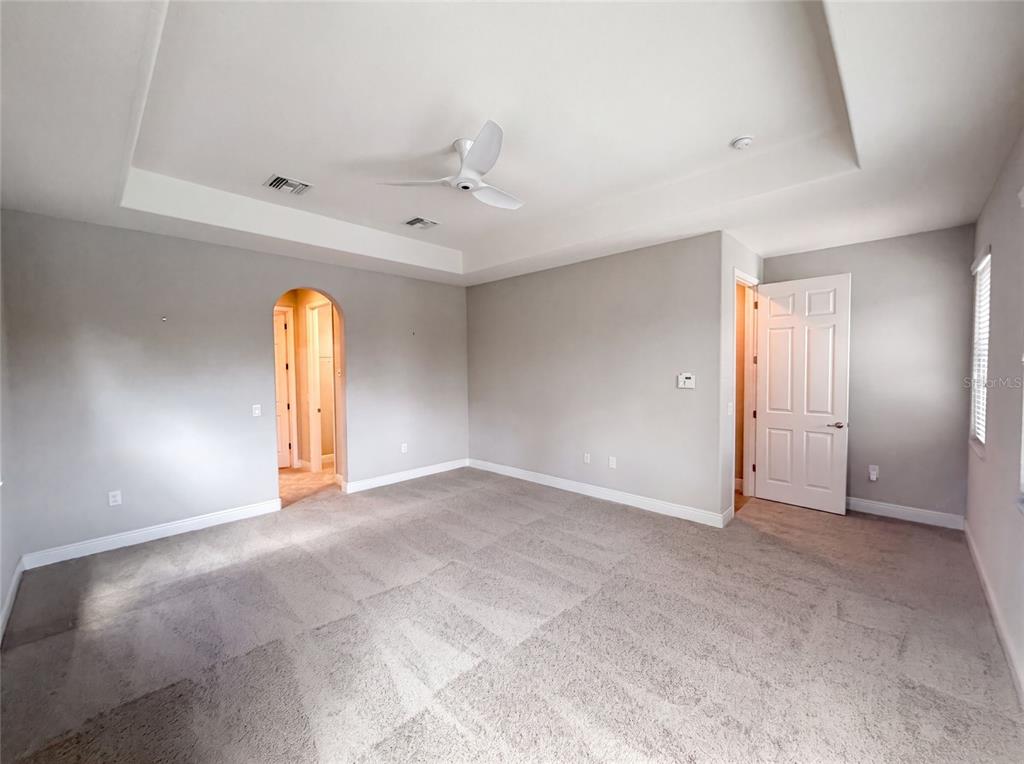 A bedroom with gray walls, carpeted flooring, a tray ceiling, and an arched doorway — 2575 GRAND LAKESIDE DRIVE, PALM HARBOR, FL