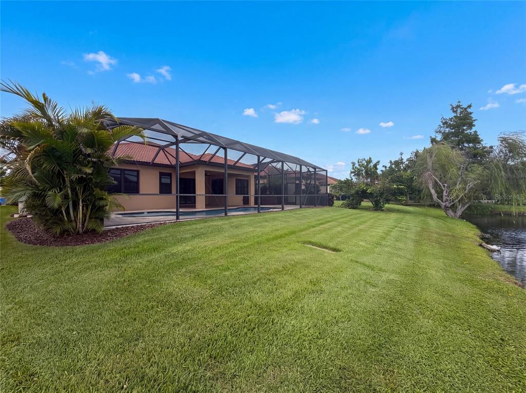A tan house with a screened-in pool enclosure sits on a grassy lawn by water — 2575 GRAND LAKESIDE DRIVE, PALM HARBOR, FL