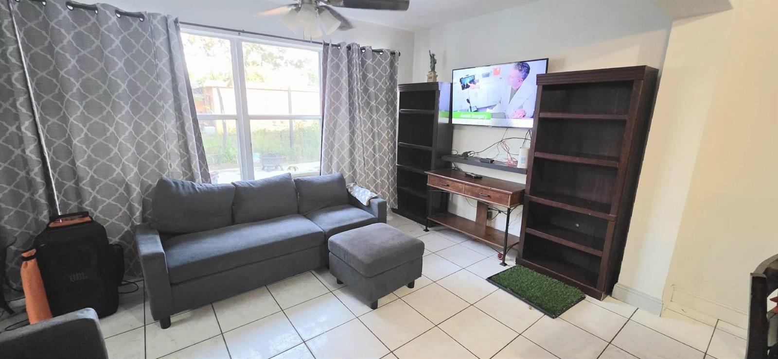 A living room features a gray sectional sofa, two dark wood bookcases, and a wall-mounted television — 2701 Arcadia Drive, Miramar FL 33023, MIRAMAR, FL