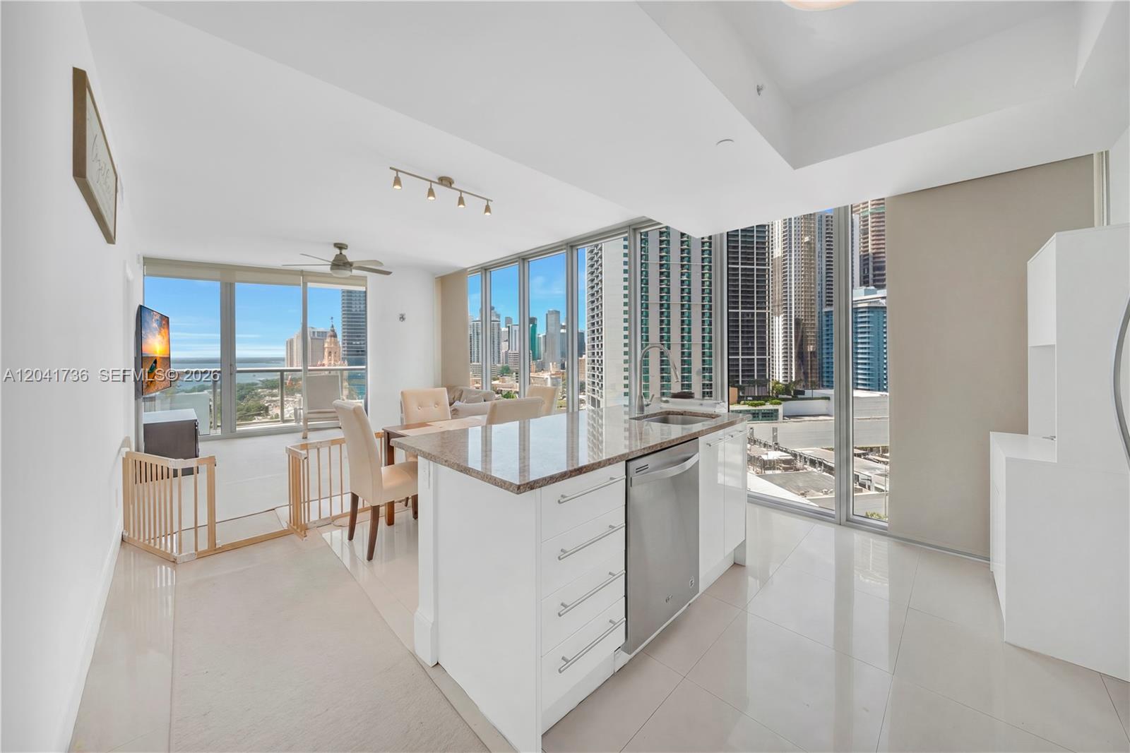 A modern kitchen with a granite island and stainless steel dishwasher overlooks a city skyline — 888 Biscayne Blvd # 2101, Miami FL 33132, MIAMI, FL