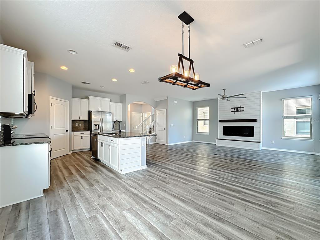 An open-concept kitchen and living area features white cabinetry, a kitchen island, and wood-look flooring — 16330 BRISK BREEZE ALLEY, WINTER GARDEN, FL