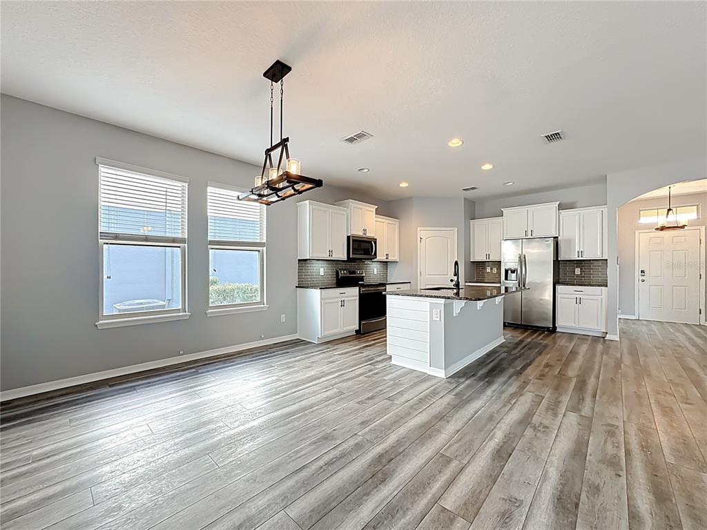 A kitchen and dining area feature white cabinets, stainless steel appliances, and wood-look flooring — 16330 BRISK BREEZE ALLEY, WINTER GARDEN, FL