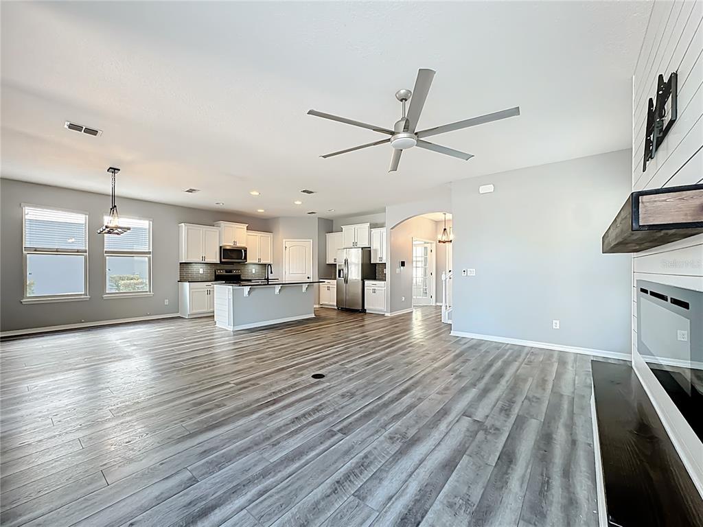 An open-concept living area features a kitchen with white cabinets, an island, and wood-look flooring — 16330 BRISK BREEZE ALLEY, WINTER GARDEN, FL