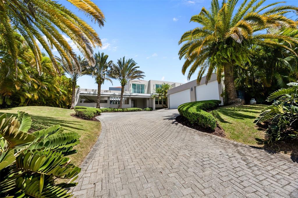 A modern house with a paved driveway, palm trees, and manicured landscaping under a blue sky — 442 DORADO BEACH EAST, DORADO, PR