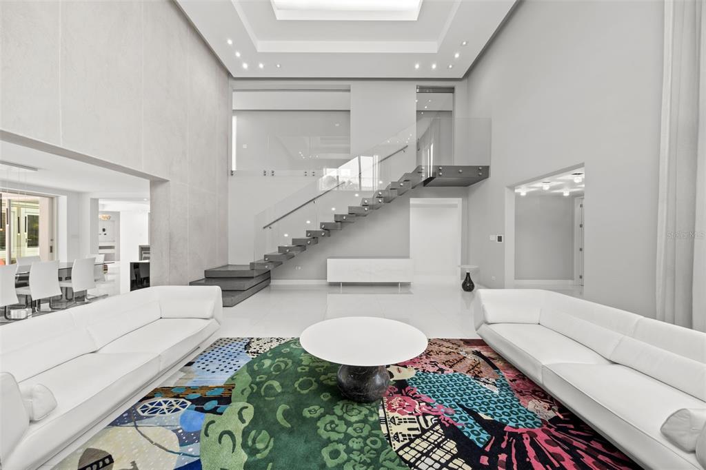 A modern living room features white sofas, a colorful area rug, and a floating staircase — 442 DORADO BEACH EAST, DORADO, PR