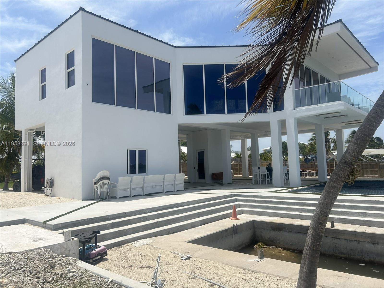 A modern white two-story house features large blue-tinted windows, a balcony, and an unfinished pool — 1553 Sunrise Dr, Big Pine FL 33043, BIG PINE, FL