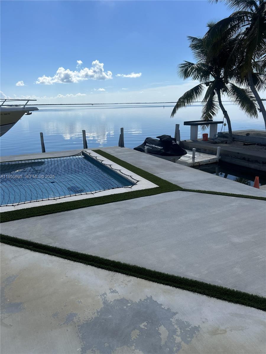 A concrete patio with a pool and a jet ski overlooks a calm bay — 1553 Sunrise Dr, Big Pine FL 33043, BIG PINE, FL