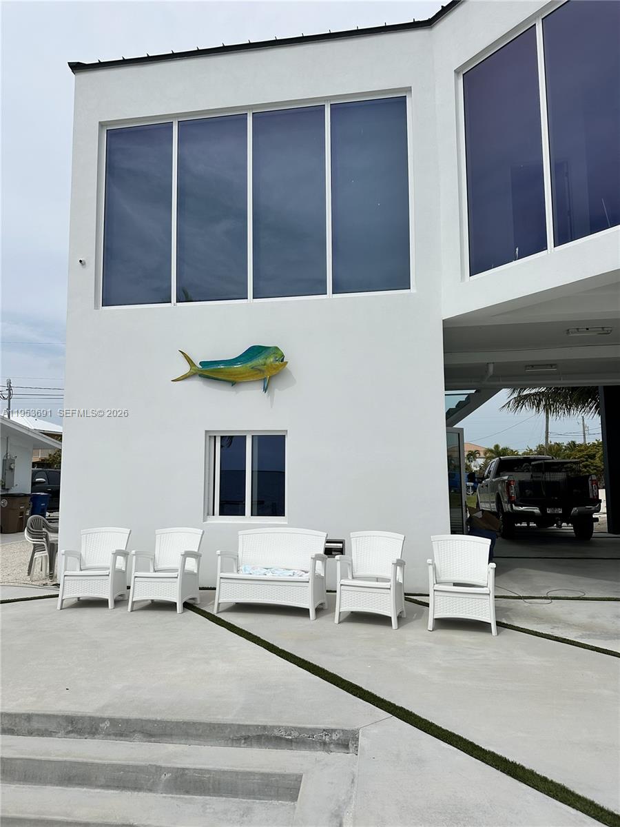 A white exterior wall features a decorative mahi-mahi fish and five white outdoor chairs — 1553 Sunrise Dr, Big Pine FL 33043, BIG PINE, FL