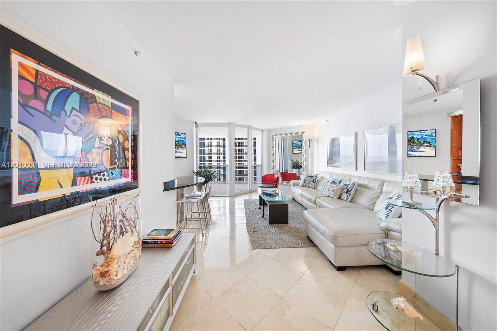 A bright living room features a white sectional sofa, tile floors, and a large colorful painting — 4779 Collins Ave # 2404, Miami Beach FL 33140, MIAMI BEACH, FL