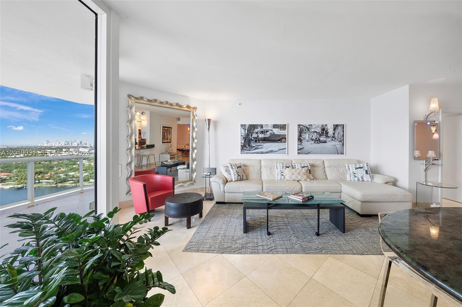 A bright living room features a white sectional sofa, a large mirror, and balcony views — 4779 Collins Ave # 2404, Miami Beach FL 33140, MIAMI BEACH, FL