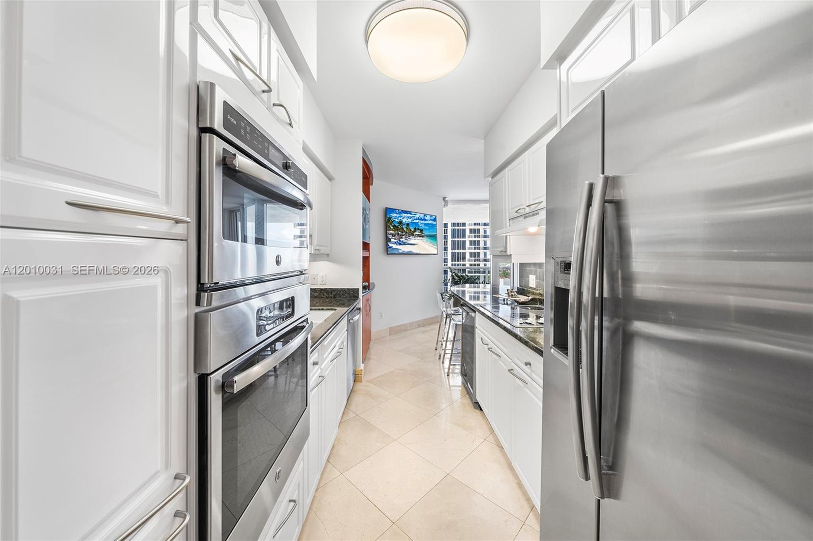 A galley kitchen features white cabinets, stainless steel appliances, and light-colored tile flooring — 4779 Collins Ave # 2404, Miami Beach FL 33140, MIAMI BEACH, FL