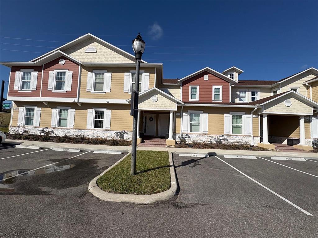 A two-story multi-family building with tan and red siding features a parking lot in front — 7595 SUNFLOWER CIRCLE, KISSIMMEE, FL