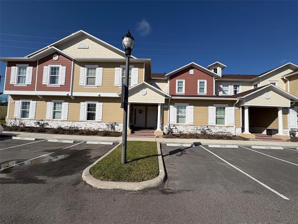 Exterior view of a two-story apartment building with tan siding, red accents, and parking spaces — 7595 SUNFLOWER CIRCLE, KISSIMMEE, FL