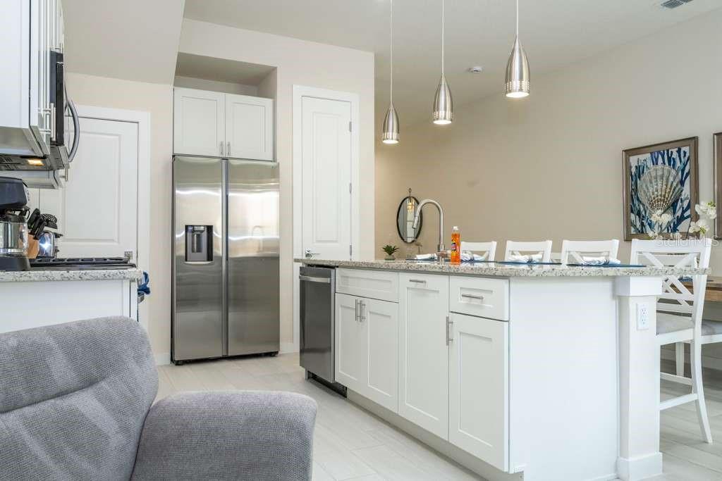 A kitchen features white cabinets, stainless steel appliances, a granite island, and three pendant lights — 7595 SUNFLOWER CIRCLE, KISSIMMEE, FL