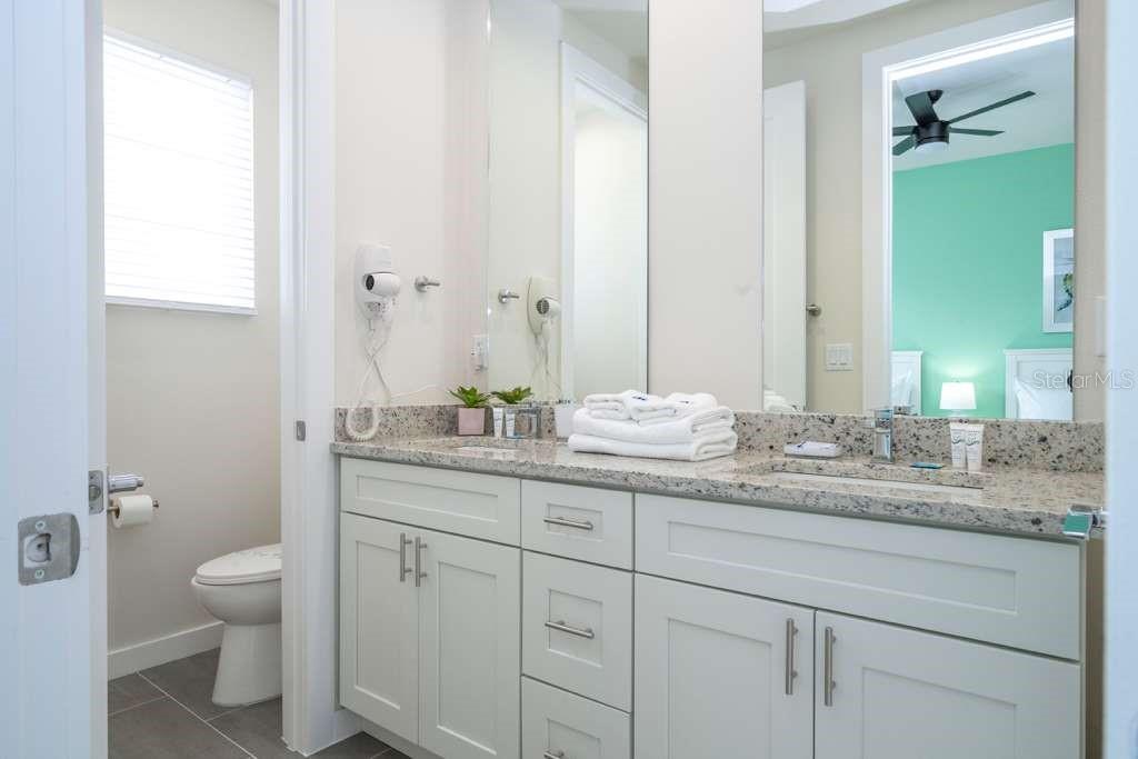 A bathroom features a double vanity with granite countertops, white cabinetry, and a separate toilet area — 7595 SUNFLOWER CIRCLE, KISSIMMEE, FL