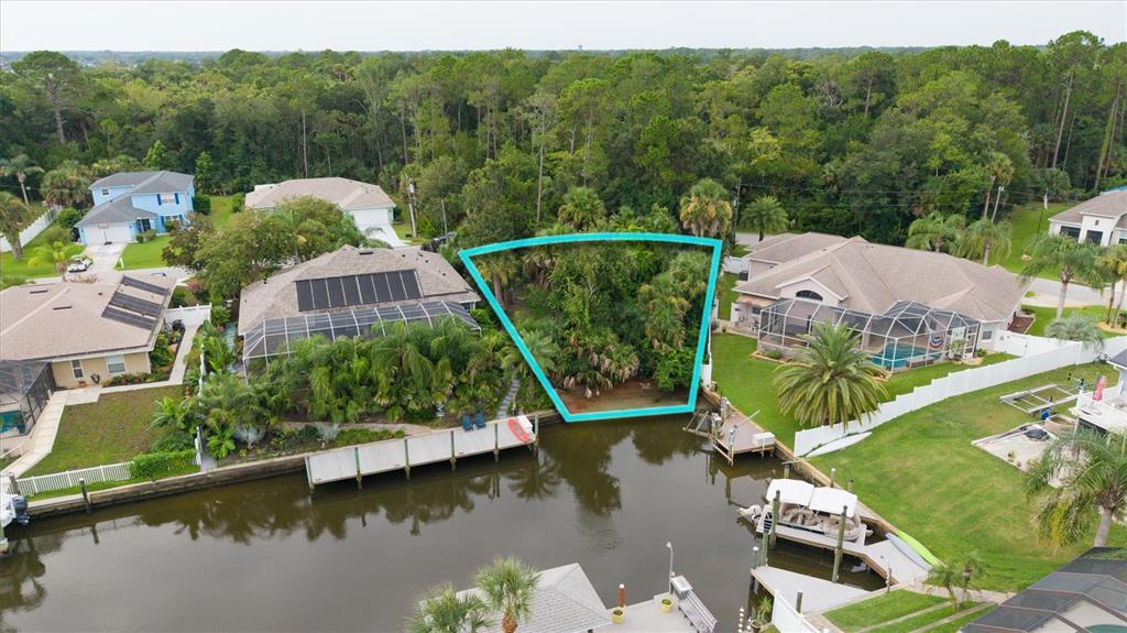 An aerial view shows a vacant, wooded waterfront lot outlined in blue between two houses — 27 COLECHESTER LANE, PALM COAST, FL