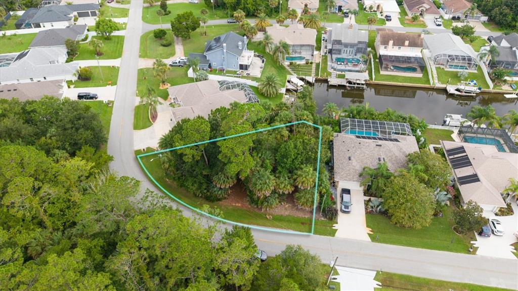 An aerial view shows a vacant, tree-covered lot outlined in blue next to a residential house — 27 COLECHESTER LANE, PALM COAST, FL