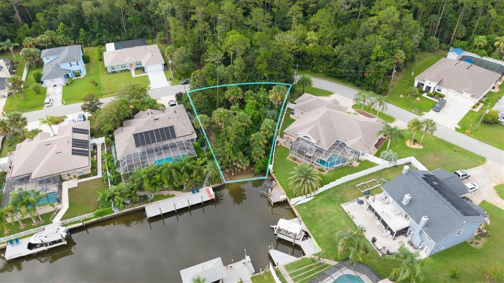 An aerial view shows a vacant, wooded waterfront lot situated between two residential homes — 27 COLECHESTER LANE, PALM COAST, FL